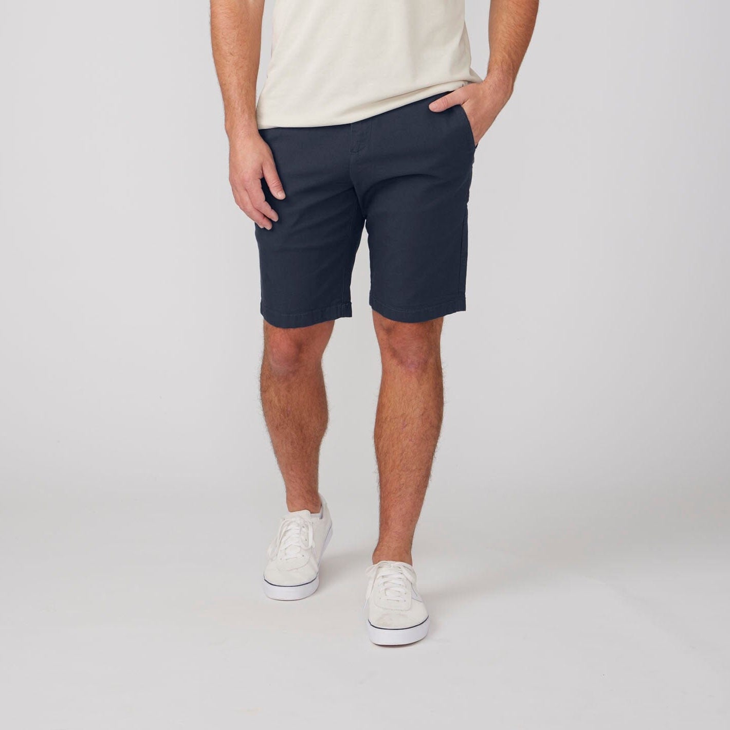 Person wearing navy shorts and white sneakers on a plain background