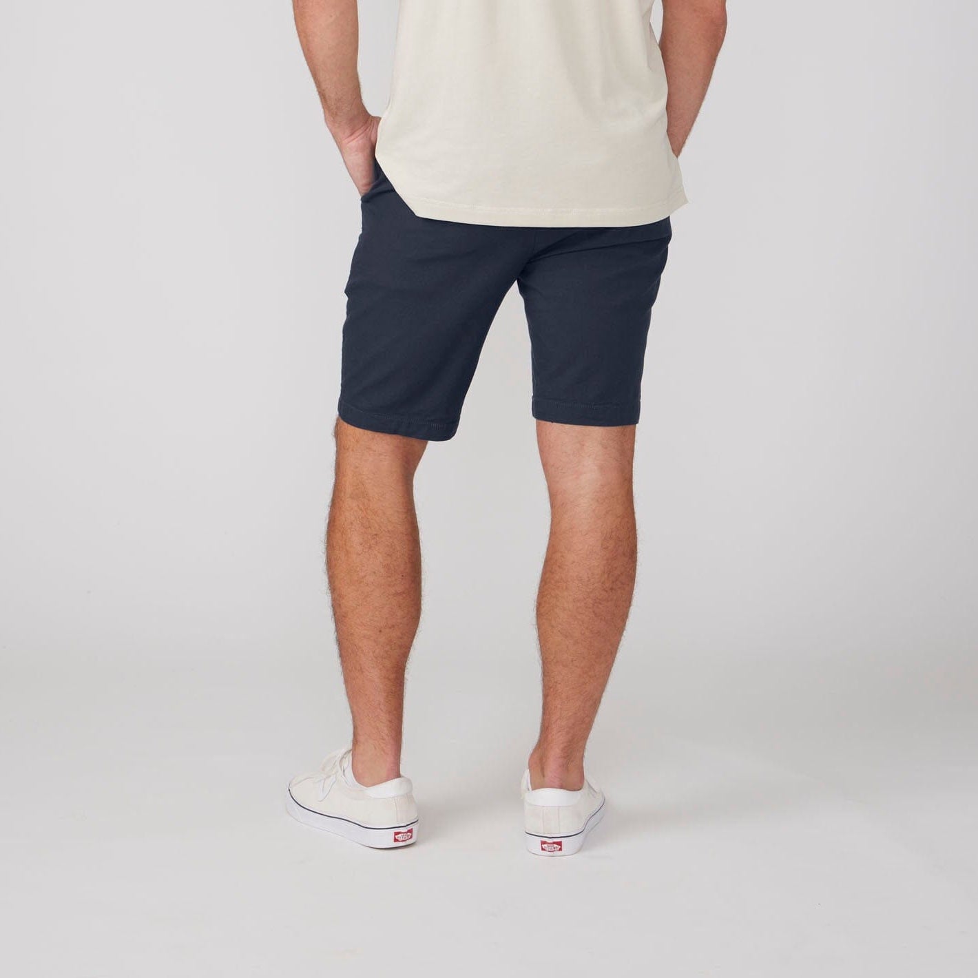 Person wearing navy shorts and white sneakers on a plain background