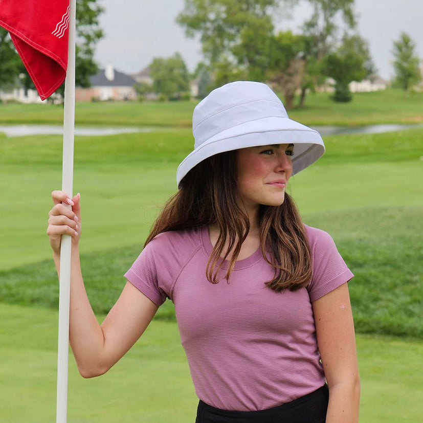 Woman in a pink shirt and white sun hat holding a red flag on a golf course
